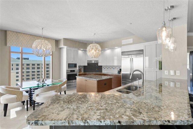 kitchen featuring backsplash, built in appliances, a sink, light stone countertops, and a notable chandelier