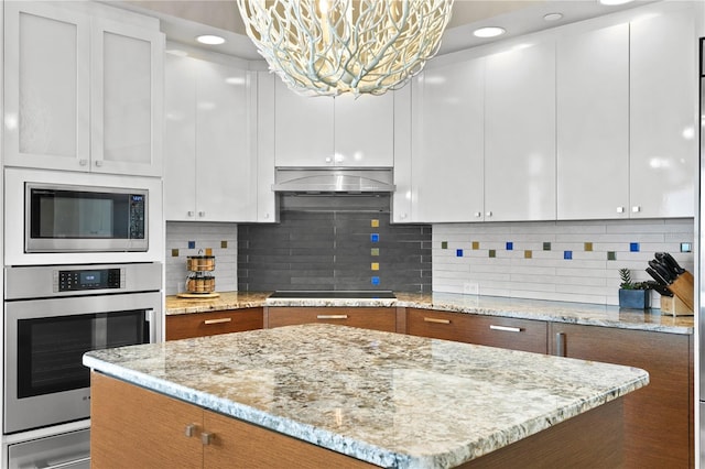 kitchen with under cabinet range hood, stainless steel appliances, decorative backsplash, and a warming drawer