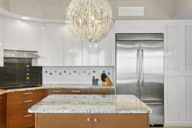 kitchen featuring built in fridge, a notable chandelier, tasteful backsplash, white cabinetry, and black electric stovetop