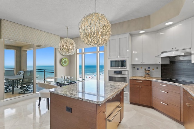 kitchen with white cabinets, a kitchen island, stainless steel appliances, under cabinet range hood, and a chandelier