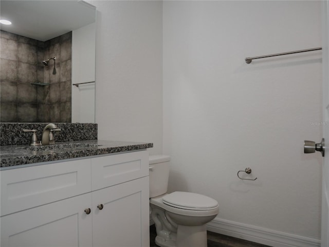 bathroom featuring tiled shower, baseboards, toilet, and vanity