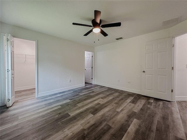 unfurnished bedroom featuring visible vents, a walk in closet, wood finished floors, baseboards, and ceiling fan