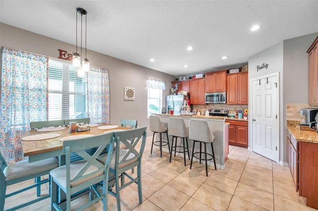 kitchen featuring hanging light fixtures, stainless steel appliances, tasteful backsplash, light tile patterned flooring, and a kitchen breakfast bar