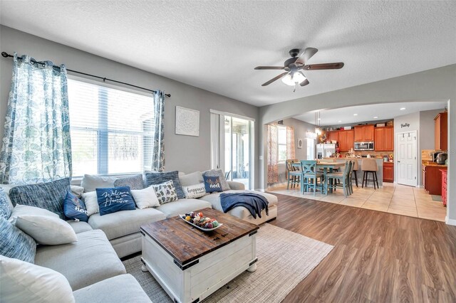 living room featuring a textured ceiling, ceiling fan, and light hardwood / wood-style floors