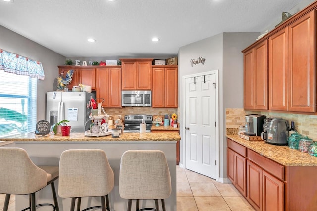 kitchen with stainless steel appliances, decorative backsplash, light tile patterned floors, and light stone countertops