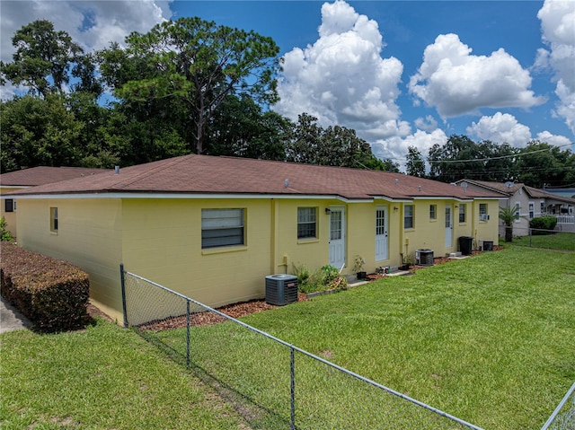 rear view of house featuring central AC unit and a yard