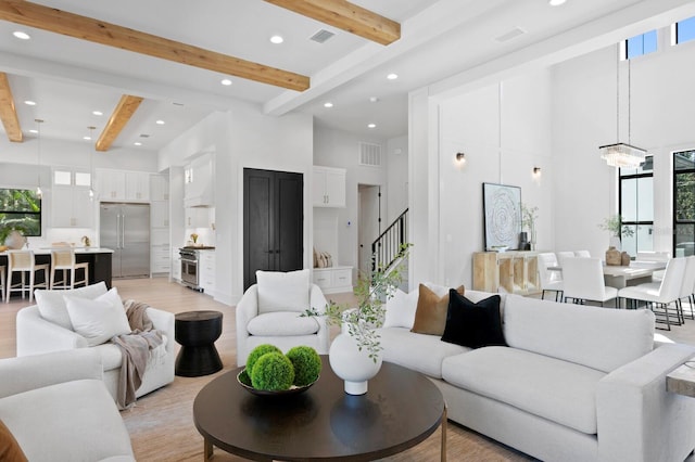 living room with beam ceiling, light hardwood / wood-style flooring, a notable chandelier, and a high ceiling