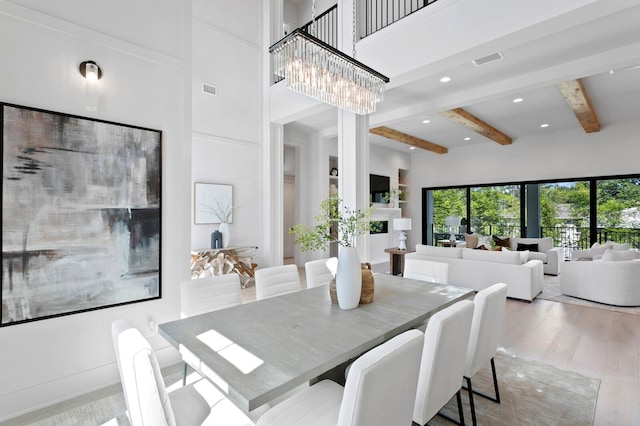 dining space featuring beamed ceiling, a high ceiling, a notable chandelier, and light hardwood / wood-style floors