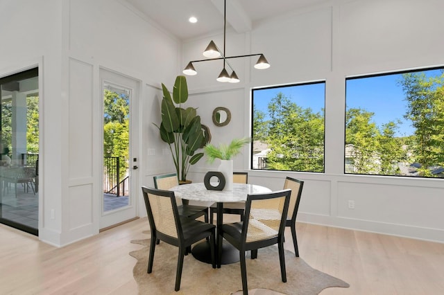 dining space with beam ceiling, a healthy amount of sunlight, light hardwood / wood-style floors, and a towering ceiling