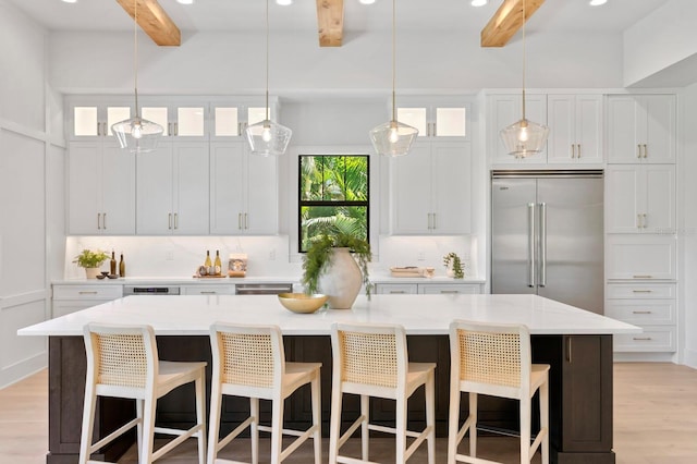 kitchen featuring beam ceiling, white cabinets, decorative light fixtures, light wood-type flooring, and stainless steel appliances