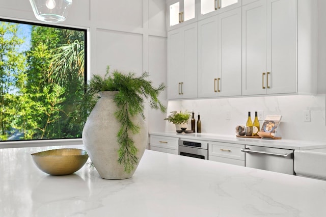 interior space featuring light stone countertops, backsplash, white cabinetry, and oven