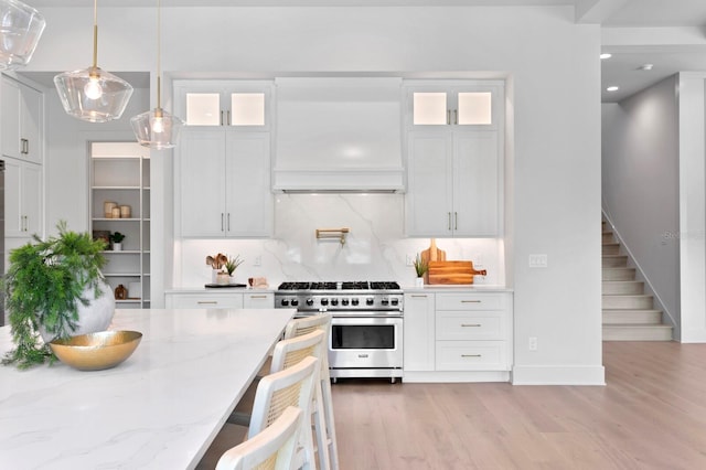 kitchen featuring backsplash, light wood-type flooring, white cabinetry, and high end stainless steel range oven