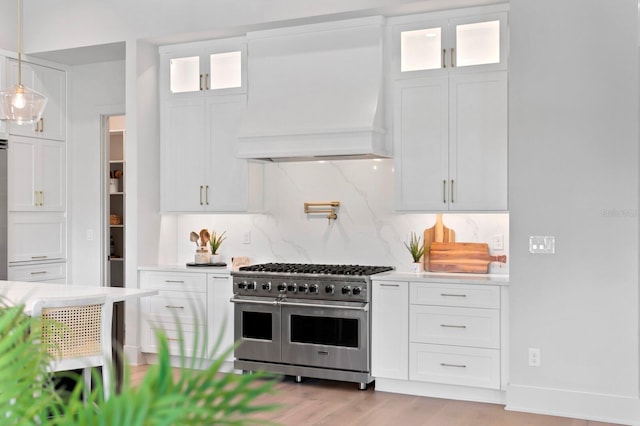 kitchen with hanging light fixtures, white cabinetry, custom exhaust hood, light hardwood / wood-style flooring, and range with two ovens