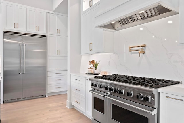 kitchen featuring white cabinets, premium appliances, light wood-type flooring, and premium range hood