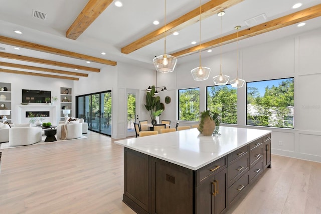 kitchen featuring light wood-type flooring, beam ceiling, a center island, dark brown cabinetry, and decorative light fixtures