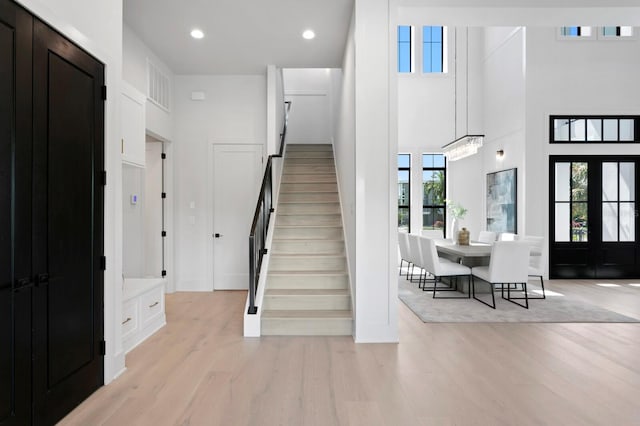 stairway featuring a towering ceiling, french doors, wood-type flooring, and a healthy amount of sunlight