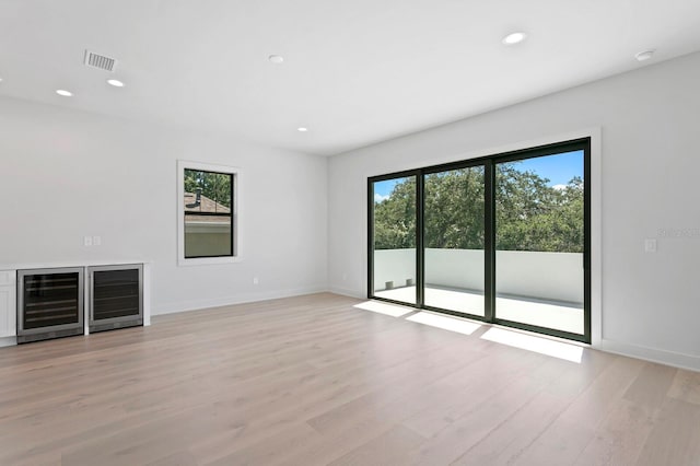 unfurnished living room featuring light hardwood / wood-style flooring, wine cooler, and a wealth of natural light