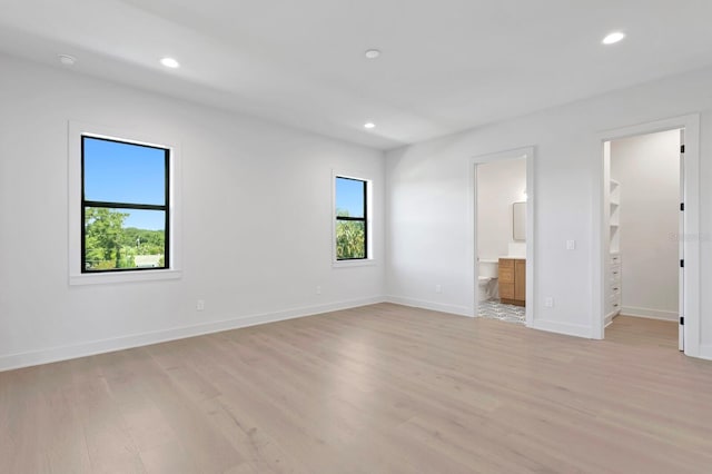 unfurnished bedroom with ensuite bathroom, light wood-type flooring, a closet, and a walk in closet