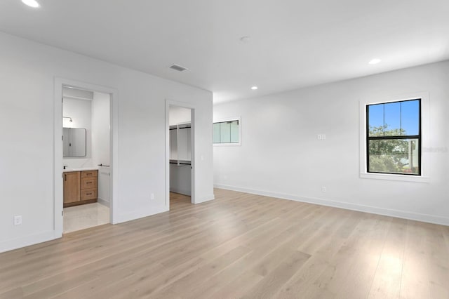 unfurnished bedroom featuring ensuite bathroom, light wood-type flooring, a spacious closet, and a closet