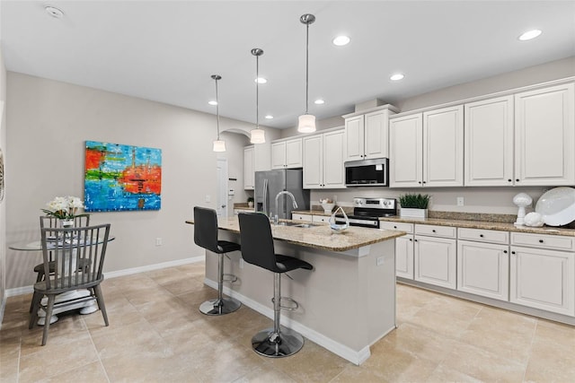 kitchen featuring light stone counters, appliances with stainless steel finishes, hanging light fixtures, a kitchen island with sink, and white cabinets