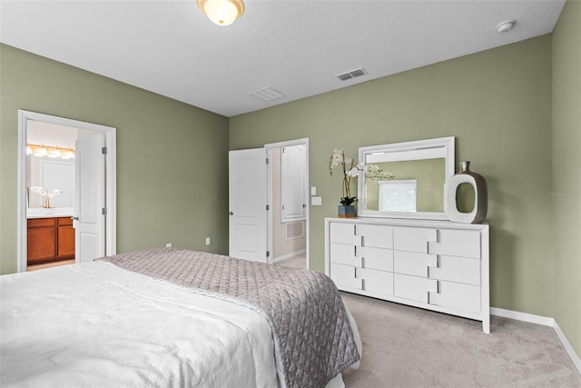 bedroom featuring a textured ceiling, ensuite bath, and light carpet