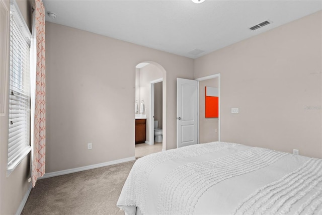 bedroom featuring ensuite bathroom and light colored carpet