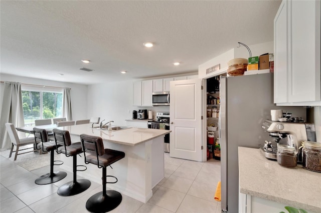 kitchen with sink, light tile patterned floors, stainless steel appliances, a kitchen breakfast bar, and white cabinets