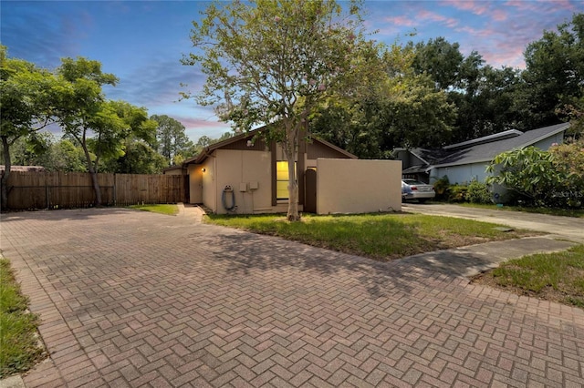 property exterior at dusk featuring fence, decorative driveway, and stucco siding