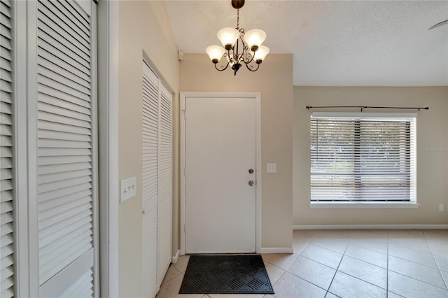 entrance foyer with light tile patterned floors, a textured ceiling, baseboards, and an inviting chandelier