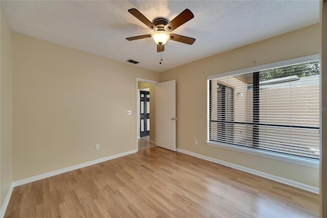 spare room featuring baseboards, visible vents, a ceiling fan, a textured ceiling, and light wood-type flooring