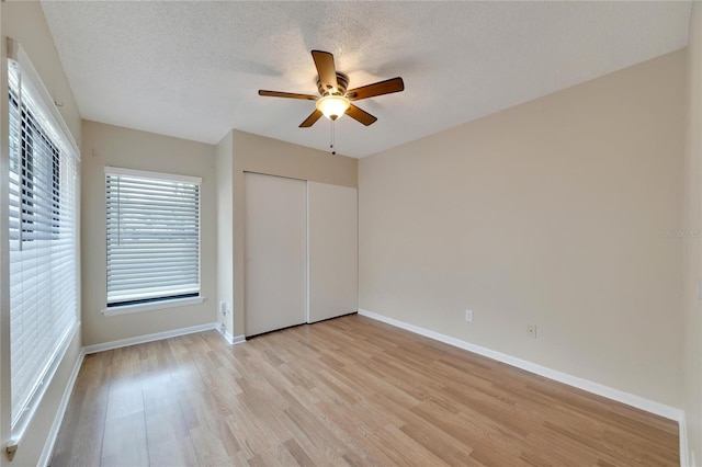 unfurnished bedroom with a closet, light wood-style flooring, ceiling fan, a textured ceiling, and baseboards