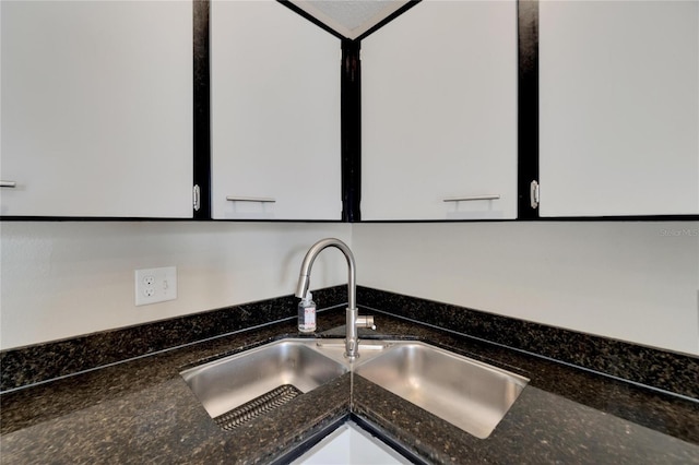 room details featuring dark stone counters, white cabinets, and a sink