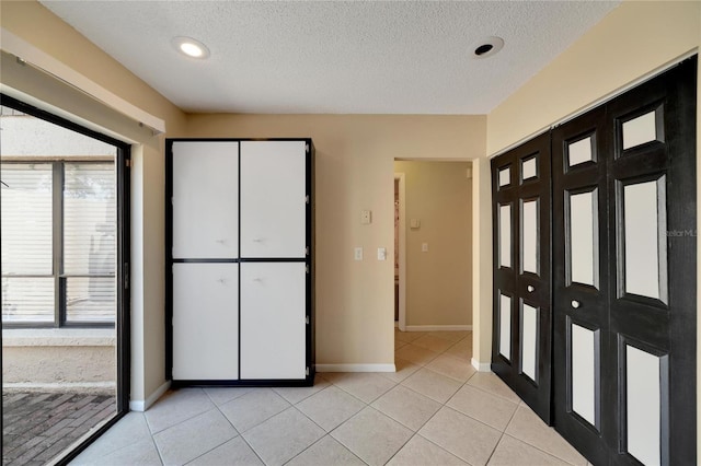 unfurnished bedroom with a textured ceiling, light tile patterned flooring, and baseboards