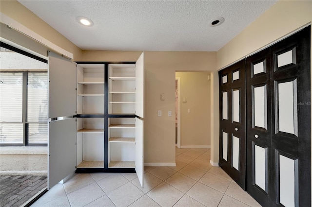 interior space with a textured ceiling, light tile patterned flooring, and baseboards