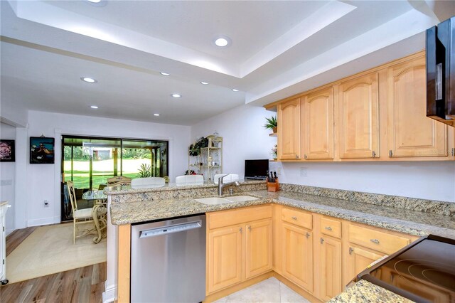 kitchen featuring stainless steel dishwasher, a tray ceiling, sink, light hardwood / wood-style flooring, and kitchen peninsula