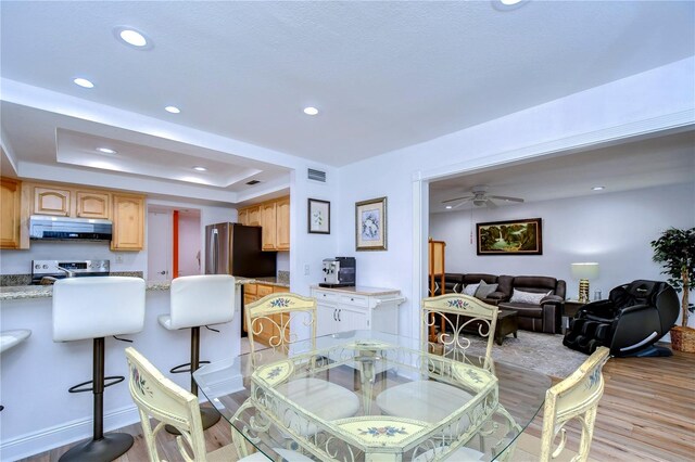 dining area with light hardwood / wood-style flooring, ceiling fan, and a raised ceiling