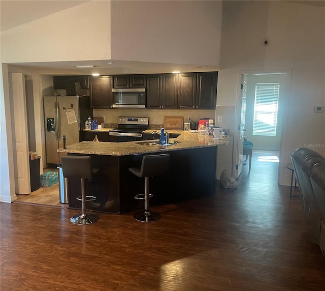 kitchen featuring appliances with stainless steel finishes, sink, light stone counters, a kitchen breakfast bar, and hardwood / wood-style flooring