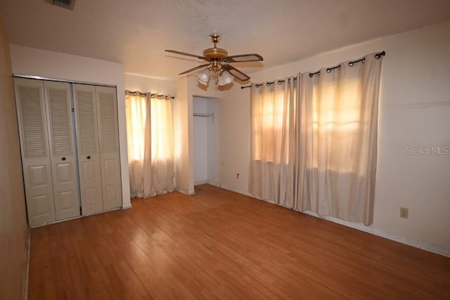 unfurnished bedroom with hardwood / wood-style floors, two closets, and ceiling fan