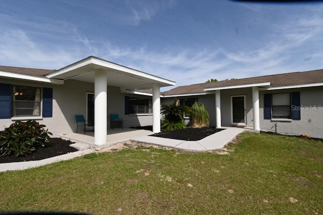 rear view of property with a patio, a yard, and stucco siding