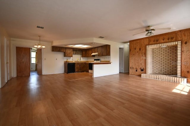 unfurnished living room with a sink, ceiling fan with notable chandelier, visible vents, and wood finished floors
