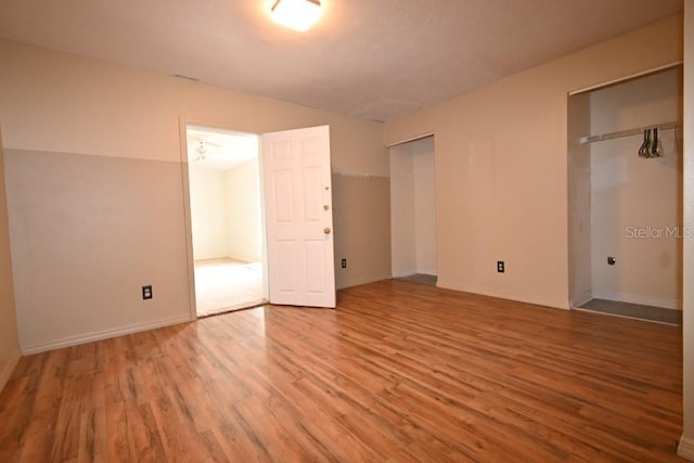 unfurnished bedroom featuring baseboards, multiple closets, and wood finished floors