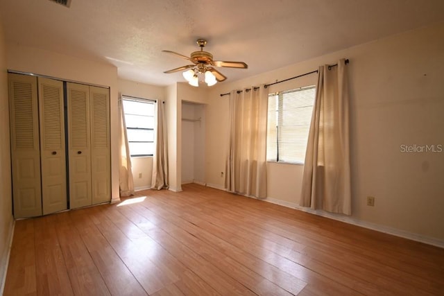 unfurnished bedroom with a ceiling fan, light wood-style flooring, baseboards, and multiple closets
