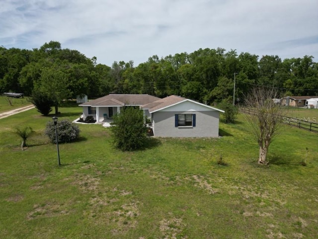 view of front facade featuring a front yard, fence, a wooded view, and stucco siding