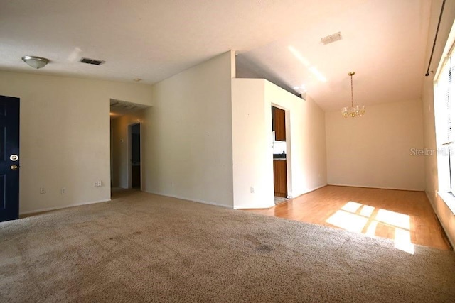 unfurnished room featuring vaulted ceiling, a notable chandelier, visible vents, and carpet floors