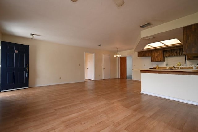 unfurnished living room with visible vents, a notable chandelier, and light wood-style flooring