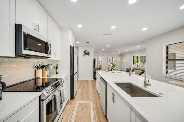 kitchen with light stone countertops, sink, stainless steel appliances, light hardwood / wood-style floors, and white cabinets