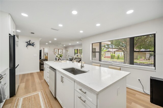 kitchen featuring white cabinets, a center island with sink, stainless steel dishwasher, and sink