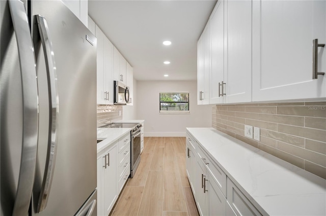 kitchen featuring white cabinetry, stainless steel appliances, tasteful backsplash, light stone counters, and light hardwood / wood-style flooring