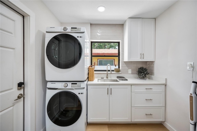 laundry area with cabinets, stacked washing maching and dryer, and sink