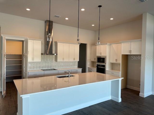 kitchen featuring sink, white cabinets, a large island, black appliances, and wall chimney exhaust hood